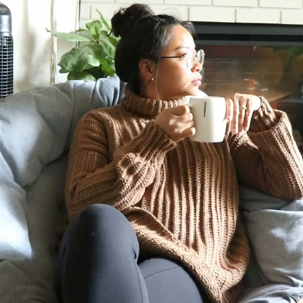a woman wearing a crochet sweater while holding a cup