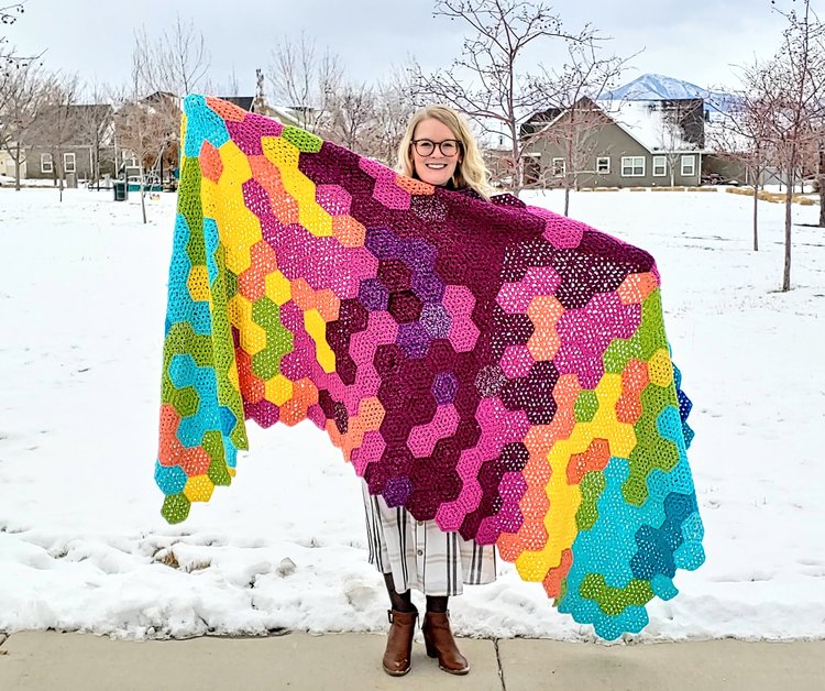 a woman holding a granny hexagon temperature crochet blanket