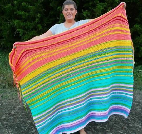 a woman holding a stripe-colored crochet blanket
